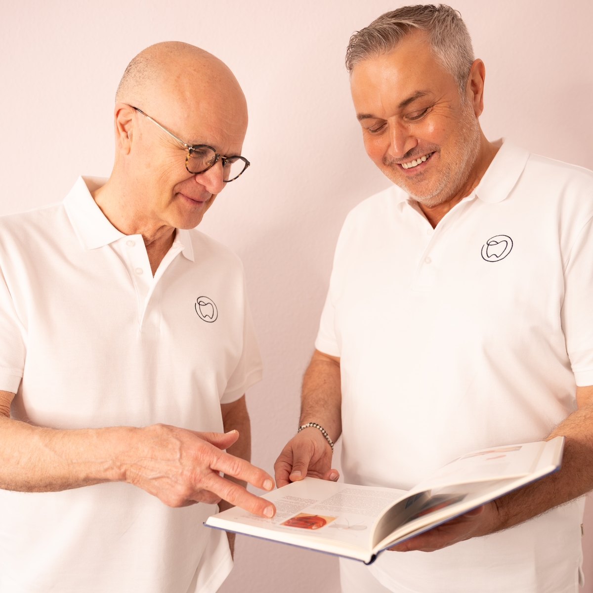 Konrad Witkowski und sein Kollege Dr. Stefan Harder sehen gemeinsam in ein Buch, in der Zahnarztpraxis in Hamburg-Wilhelmsburg